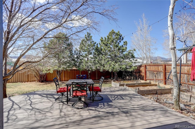 wooden terrace featuring a garden, outdoor dining area, and a fenced backyard