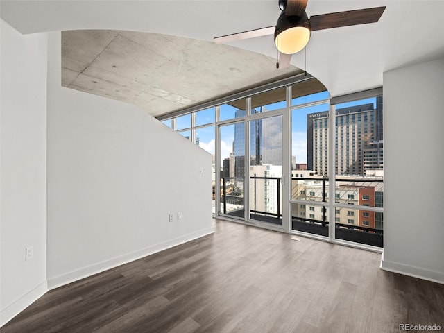 empty room with wood finished floors, baseboards, ceiling fan, floor to ceiling windows, and a city view