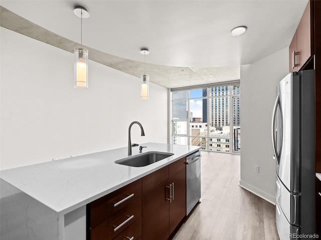 kitchen featuring a center island with sink, a sink, light wood-style flooring, hanging light fixtures, and stainless steel appliances
