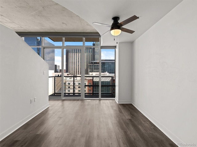 empty room with baseboards, ceiling fan, a city view, and wood finished floors