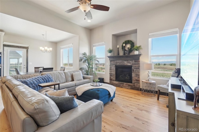 living area with a stone fireplace, wood finished floors, and ceiling fan with notable chandelier