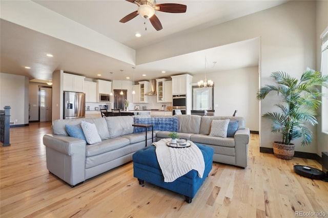 living area with light wood-style floors, ceiling fan with notable chandelier, and recessed lighting