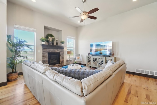 living area with visible vents, ceiling fan, a stone fireplace, and light wood-type flooring