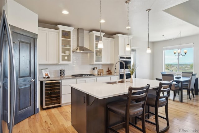 kitchen with wall chimney range hood, decorative backsplash, light countertops, wine cooler, and stainless steel appliances