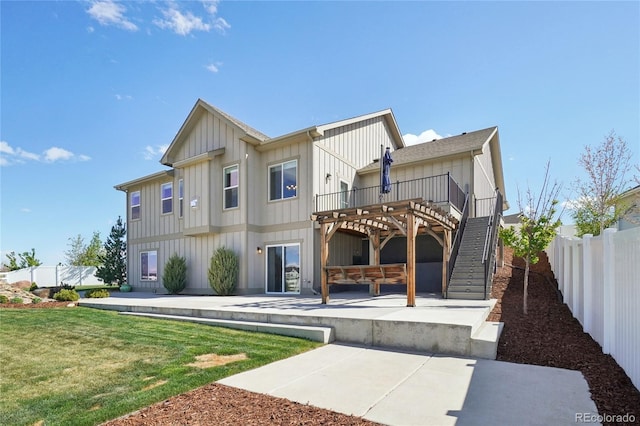 rear view of property featuring board and batten siding, a wooden deck, stairway, fence, and a patio