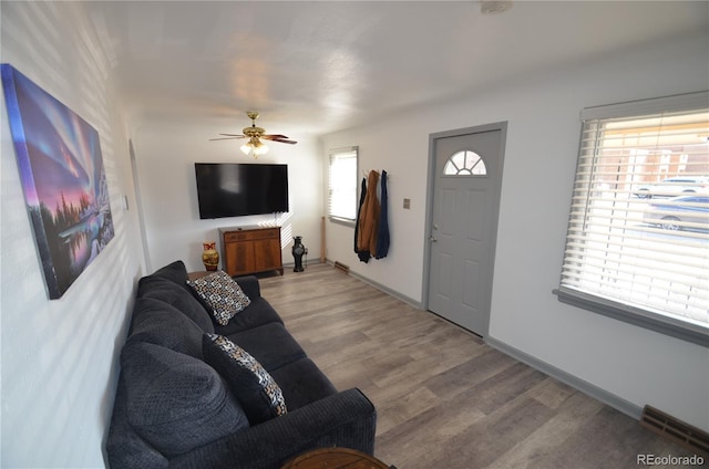 living room featuring light wood-style flooring, baseboards, a ceiling fan, and visible vents