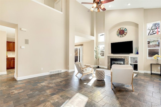 living room with ceiling fan, a fireplace, and a high ceiling