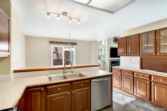 kitchen with sink, an inviting chandelier, a stone fireplace, stainless steel dishwasher, and pendant lighting