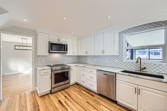 kitchen with appliances with stainless steel finishes, white cabinets, light stone countertops, light hardwood / wood-style flooring, and sink