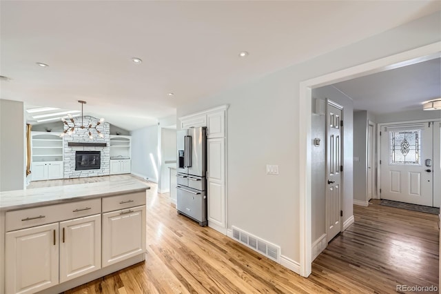 kitchen featuring white cabinetry, light hardwood / wood-style floors, a stone fireplace, high quality fridge, and vaulted ceiling