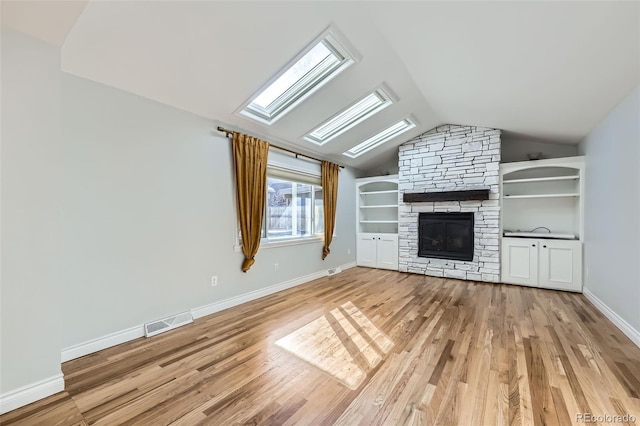 unfurnished living room with light hardwood / wood-style floors, lofted ceiling with skylight, and a stone fireplace