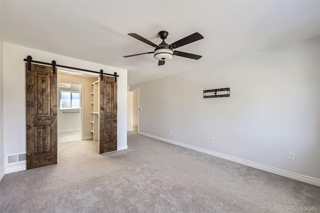 unfurnished bedroom featuring ceiling fan, light colored carpet, and a barn door