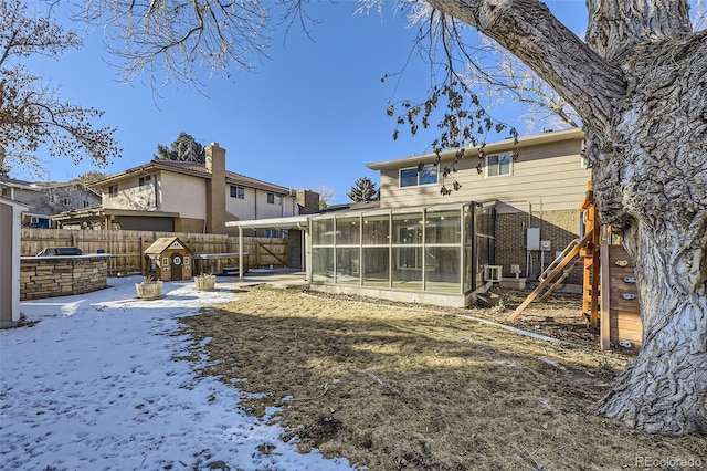 snow covered rear of property with a sunroom