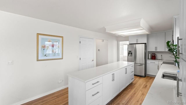 kitchen featuring stainless steel fridge, a kitchen island, light countertops, light wood-style floors, and backsplash