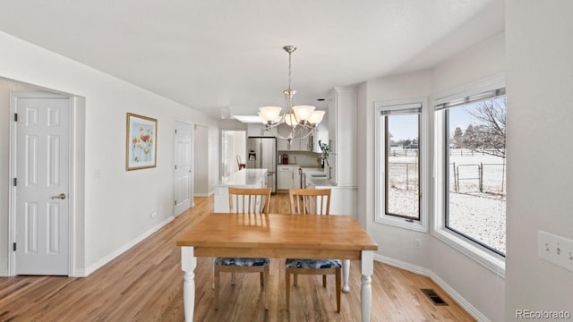 dining room featuring baseboards, visible vents, a notable chandelier, and light wood finished floors