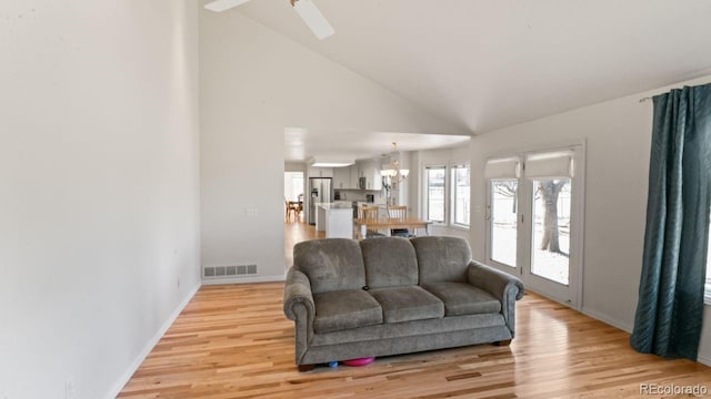 living room featuring light wood finished floors, baseboards, visible vents, high vaulted ceiling, and ceiling fan with notable chandelier