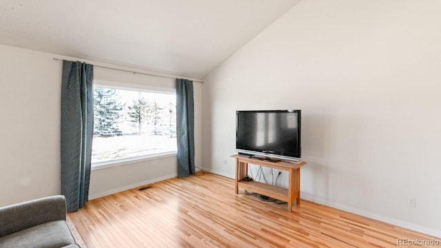 living area featuring lofted ceiling, visible vents, baseboards, and wood finished floors