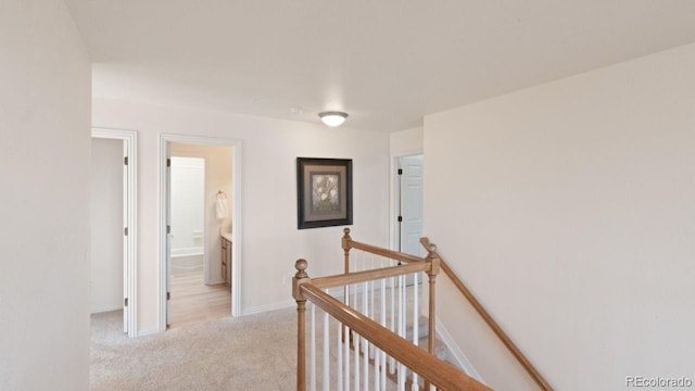 hallway featuring baseboards, an upstairs landing, and light colored carpet