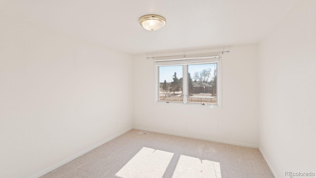 spare room featuring light colored carpet and baseboards