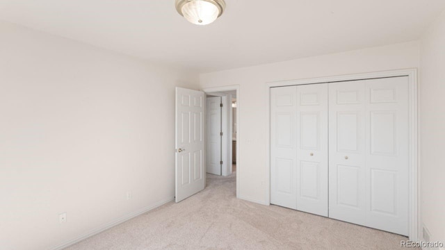 unfurnished bedroom with light carpet, baseboards, and a closet