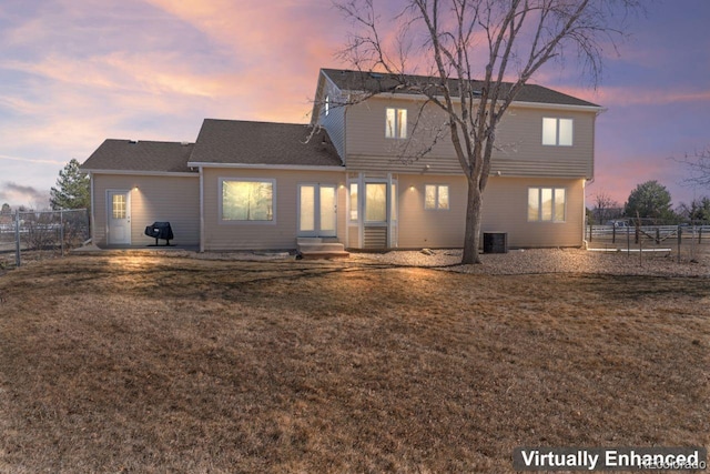 back of house at dusk featuring entry steps, a lawn, fence, and central air condition unit