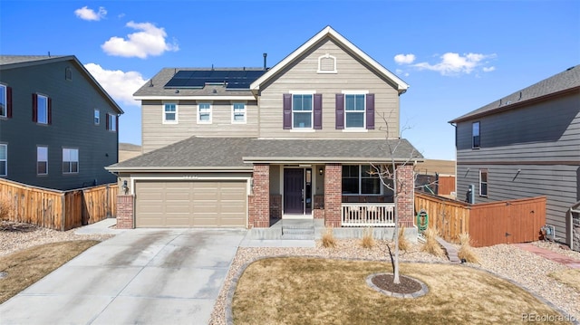 traditional home featuring solar panels, concrete driveway, fence, a porch, and brick siding