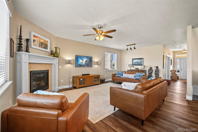 living room featuring a tile fireplace, dark wood-style flooring, ceiling fan, and baseboards