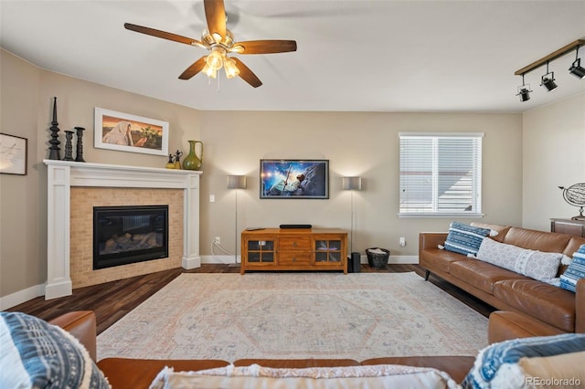 living area featuring a fireplace, rail lighting, a ceiling fan, wood finished floors, and baseboards