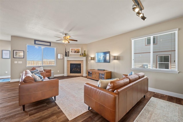 living area featuring a tile fireplace, dark wood-style flooring, a ceiling fan, visible vents, and baseboards