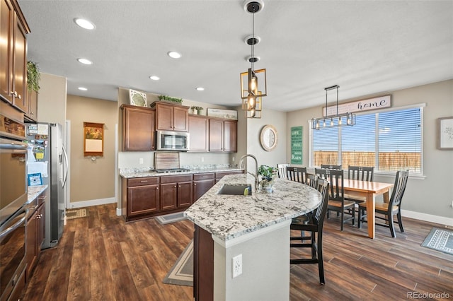 kitchen featuring a breakfast bar area, stainless steel appliances, dark wood-type flooring, a kitchen island with sink, and a sink