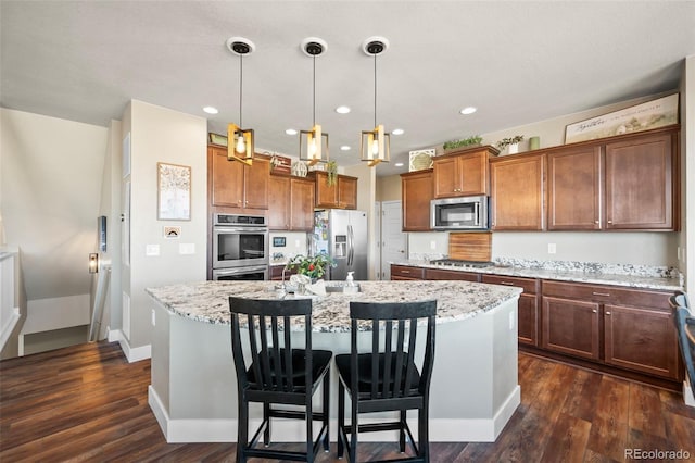 kitchen with light stone counters, stainless steel appliances, an island with sink, dark wood finished floors, and decorative light fixtures