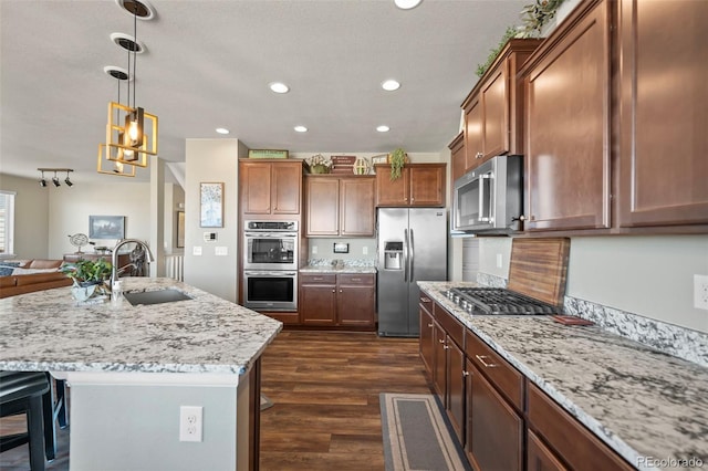 kitchen featuring dark wood-style floors, light stone counters, appliances with stainless steel finishes, open floor plan, and a sink