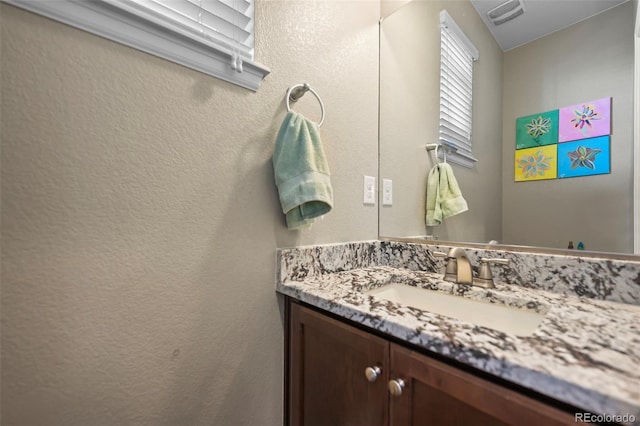 bathroom featuring visible vents, a textured wall, and vanity