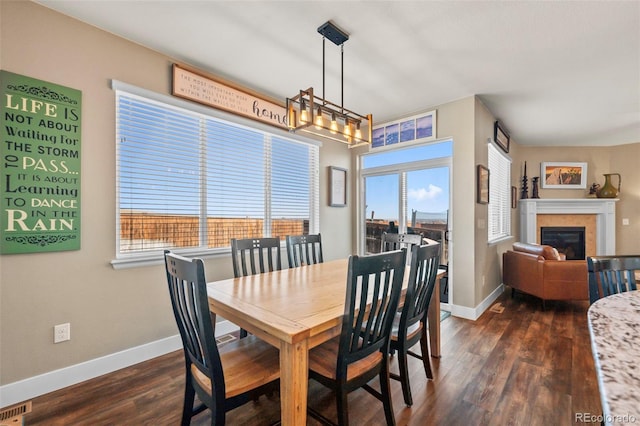 dining room with dark wood-style flooring, visible vents, baseboards, a wealth of natural light, and a glass covered fireplace