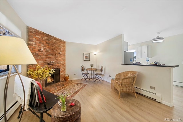 living room featuring a baseboard heating unit, a brick fireplace, plenty of natural light, and light hardwood / wood-style flooring