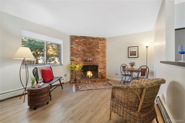 living area with baseboard heating, a brick fireplace, and light hardwood / wood-style flooring