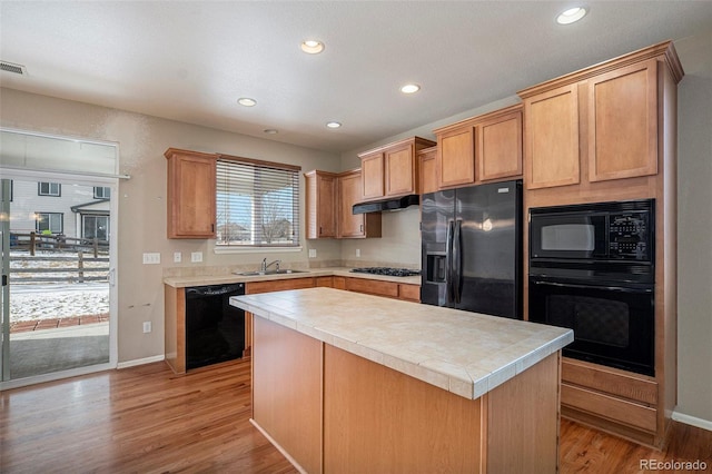 kitchen with a center island, under cabinet range hood, light countertops, black appliances, and a sink