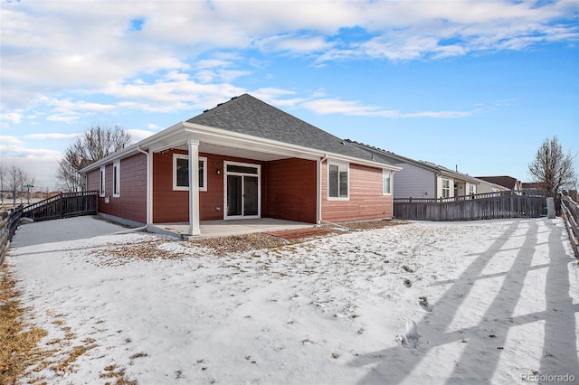 snow covered property with a patio area, fence, and roof with shingles