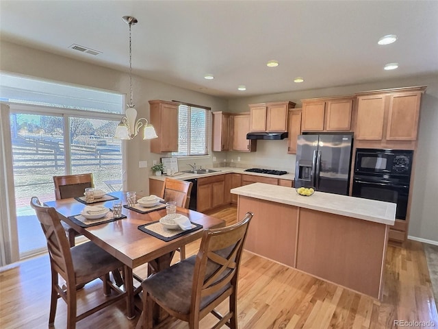 kitchen featuring light countertops, hanging light fixtures, visible vents, under cabinet range hood, and black appliances