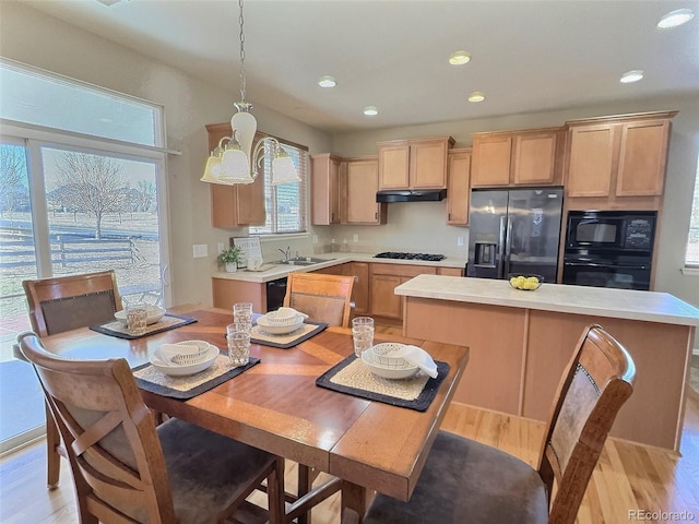 kitchen featuring hanging light fixtures, black appliances, under cabinet range hood, and light countertops