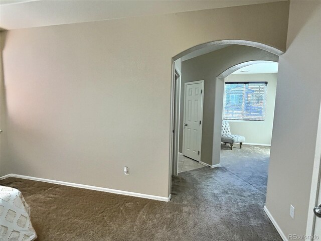 interior space with baseboards, arched walkways, and dark colored carpet