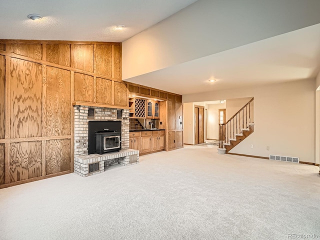 unfurnished living room with light colored carpet, wooden walls, and a wood stove