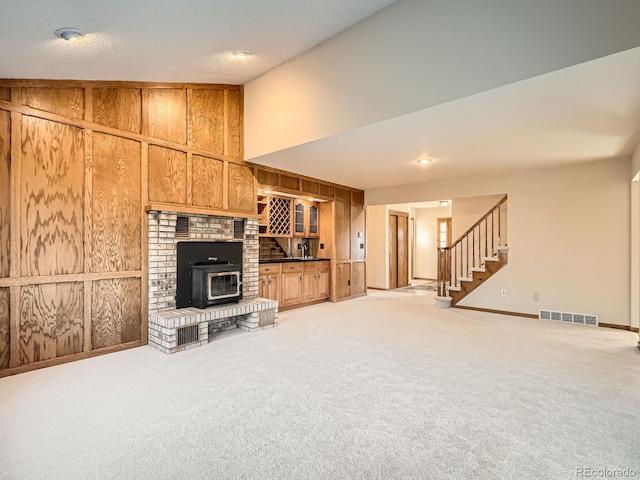 unfurnished living room featuring wooden walls, stairway, light carpet, a wood stove, and a towering ceiling