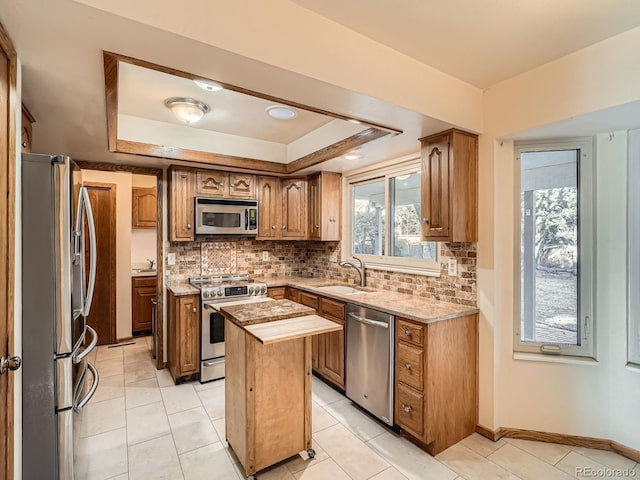 kitchen with appliances with stainless steel finishes, a center island, a sink, brown cabinets, and a tray ceiling