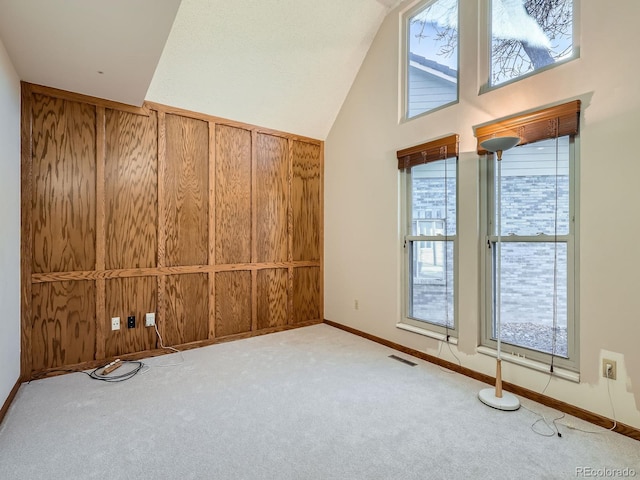 carpeted spare room featuring wooden walls, baseboards, and high vaulted ceiling