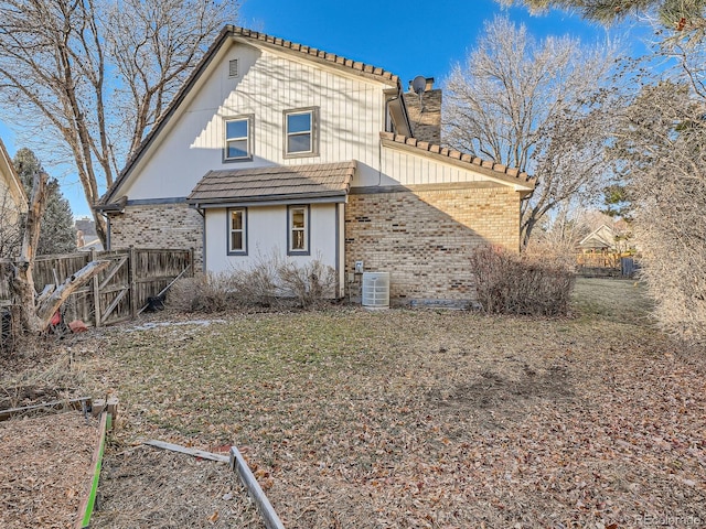 rear view of property with brick siding, a chimney, cooling unit, and fence
