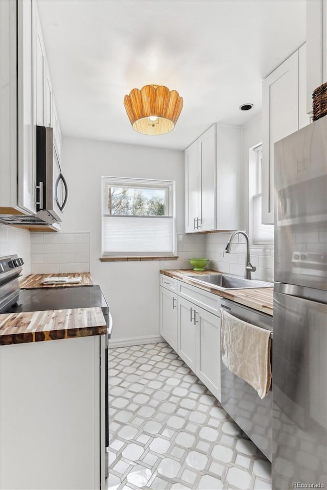 kitchen featuring appliances with stainless steel finishes, backsplash, butcher block counters, light floors, and a sink