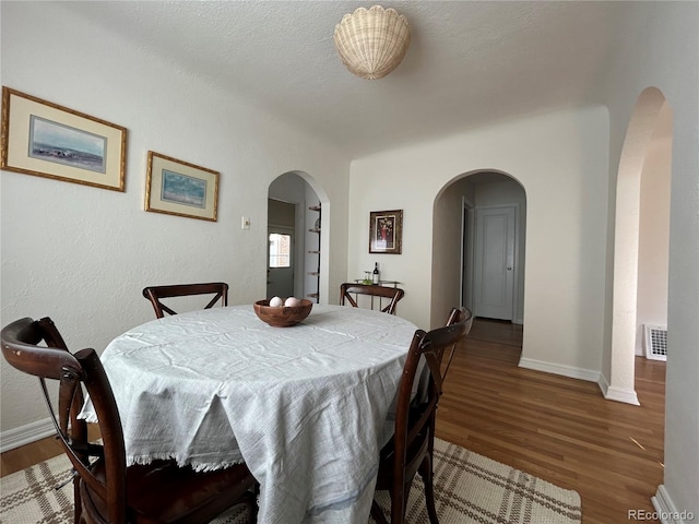 dining area with visible vents, baseboards, arched walkways, and wood finished floors
