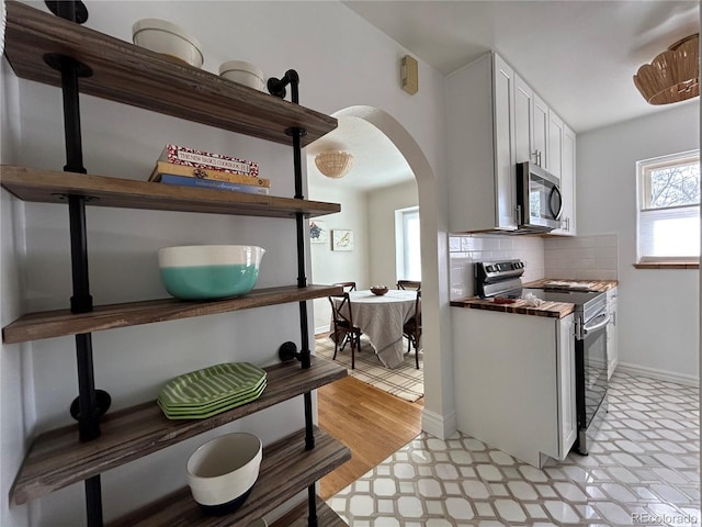 kitchen featuring tasteful backsplash, arched walkways, white cabinetry, stainless steel appliances, and light floors