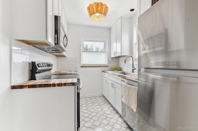 kitchen with light floors, a sink, stainless steel appliances, wood counters, and decorative backsplash